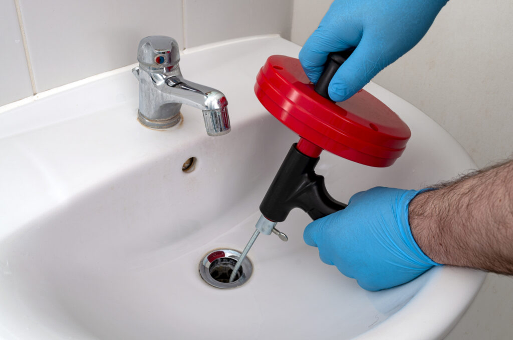 Plumber with blue gloves snaking bathroom sink drain